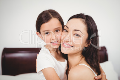 Portrait of mother smiling while hugging daughter on bed