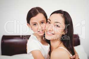 Portrait of mother smiling while hugging daughter on bed