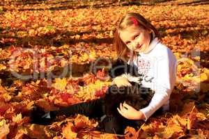 little girl plays with her cat in the autumn park