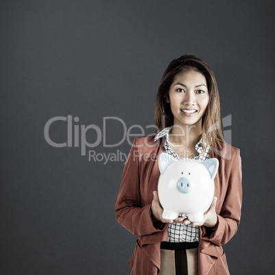 Composite image of smiling businesswoman holding a piggy bank
