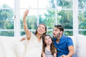Woman clicking selfie with family on sofa