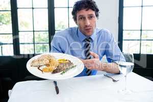 Frustrated man holding a plate of meal in restaurant