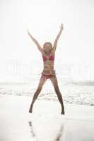 Excited woman in bikini jumping on the beach