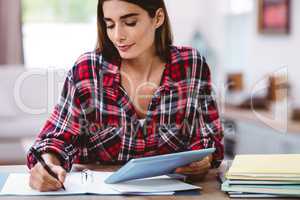 Pretty woman writing in notepad while holding digital tablet