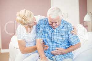 Wife comforting senior husband suffering from stomach pain