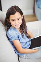 Girl using digital tablet while sitting on sofa at home