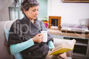 Mature woman reading book and holding coffee mug