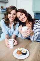 Smiling female friends holding coffee mugs at table