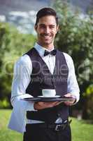 Handsome waiter holding a tray with cup of coffee