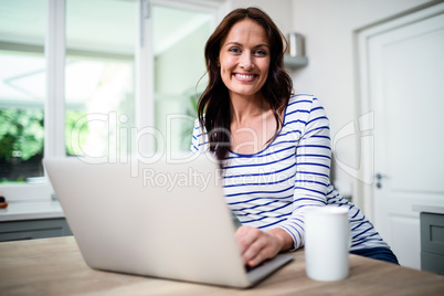 Portrait of happy woman working on laptop while holding coffee m