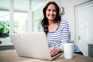 Portrait of happy woman working on laptop while holding coffee m