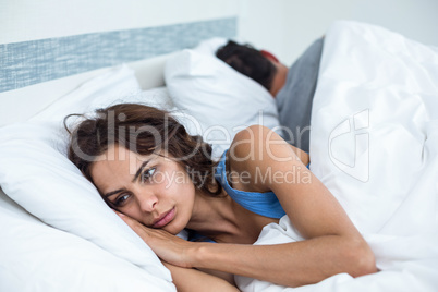 Thoughtful young woman besides husband in background lying on be