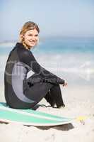 Portrait of woman in wetsuit sitting with surfboard on the beach