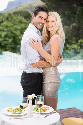 Smiling couple hugging while standing by swimming pool