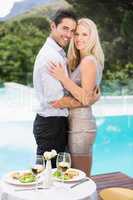 Smiling couple hugging while standing by swimming pool