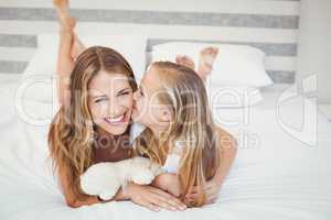 Happy daughter kissing mother while resting on bed