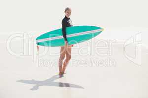 Woman in wetsuit holding a surfboard on the beach