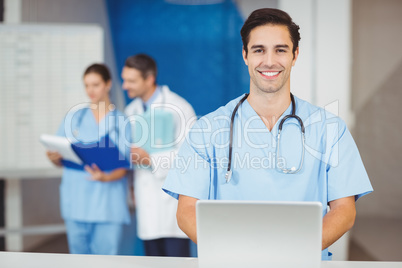 Portrait of happy doctor with laptop and colleagues discussing