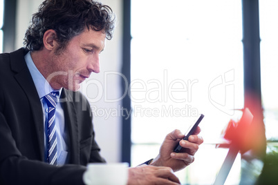 Businessman using phone while working on laptop