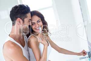 Wife brushing teeth while husband embracing her