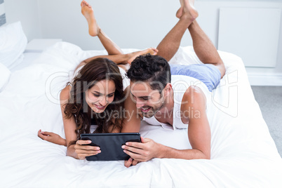 Smiling couple using digital tablet while lying under blanket