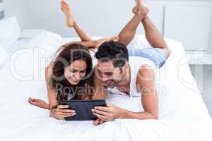 Smiling couple using digital tablet while lying under blanket