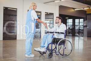 Smiling female doctor handshaking with doctor sitting on wheelch