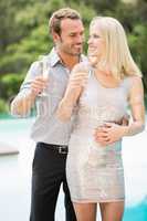 Smiling couple holding champagne flutes at poolside