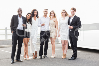 Well dressed people posing next to a limousine