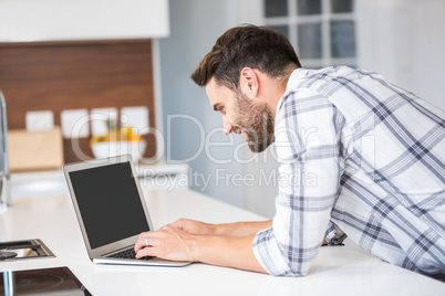 Man using laptop while leaning on kitchen counter
