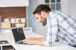 Man using laptop while leaning on kitchen counter