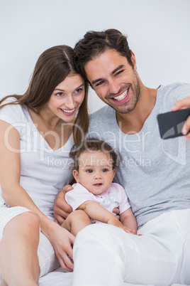 Couple clicking selfie with baby on bed