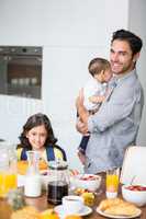 Smiling father and daughter with baby at breakfast table