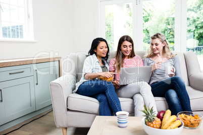 Young female friends looking in laptop at home