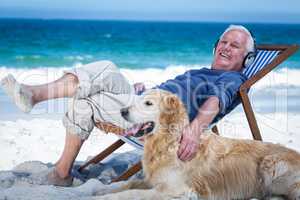 Mature man resting on a deck chair listening to music petting hi