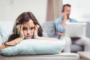 Upset girl lying on sofa while father sitting in background