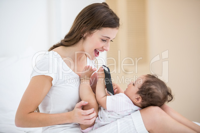 Smiling mother playing with baby holding mobile phone