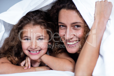 Portrait of mother and daughter lying under a white blanket