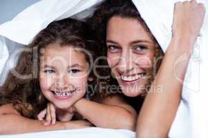 Portrait of mother and daughter lying under a white blanket
