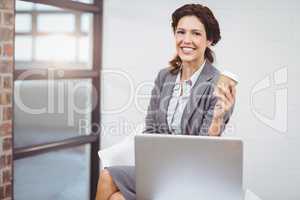 Businesswoman holding disposable cup sitting on desk