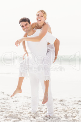 Man giving a piggy back to woman on the beach