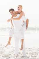 Man giving a piggy back to woman on the beach