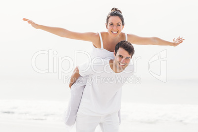 Man giving a piggy back to woman on the beach