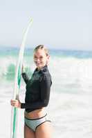 Woman in wetsuit holding a surfboard on the beach