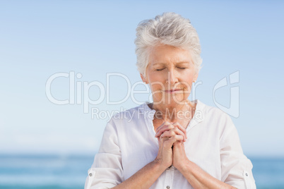 Senior woman praying on the beach