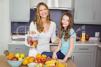Portrait of happy mother and daughter preparing fruit juice
