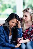 Young woman consoling depressed female friend at home