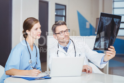 Doctor examining X-ray with colleague sitting at desk