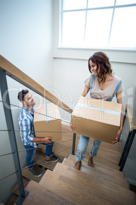 Happy couple holding cardboard boxes while climbing steps