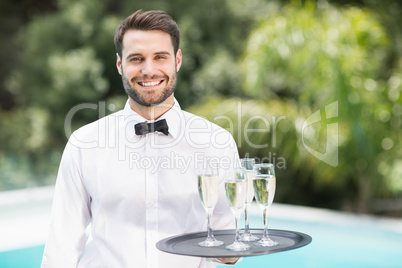 Smiling waiter carrying champagne flutes on tray